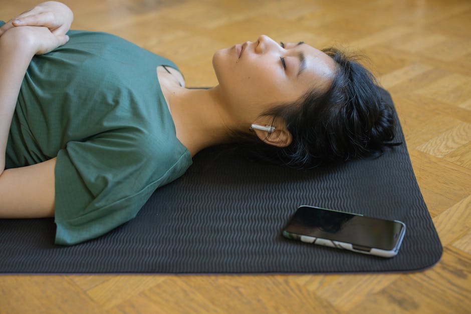 Calm vs Headspace: Sleep Meditation Effectiveness Showdown (2024) Asian woman resting on yoga mat with wireless earbuds and smartphone indoors.