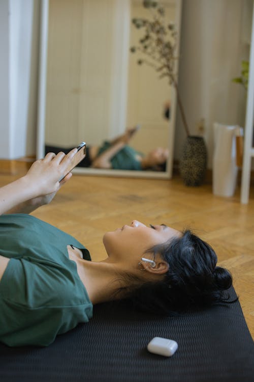 A Woman Lying on the Yoga Mat while using a Smartphone