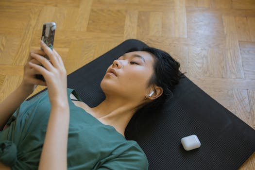 Asian woman lying on yoga mat using smartphone with AirPods in ears