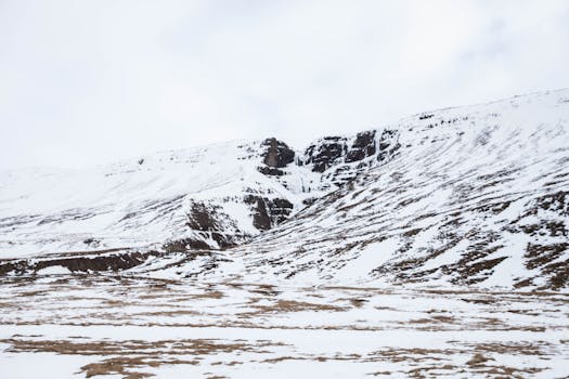 Serene snowy landscape in Búðardalur, Iceland featuring rugged mountains and vast open space.