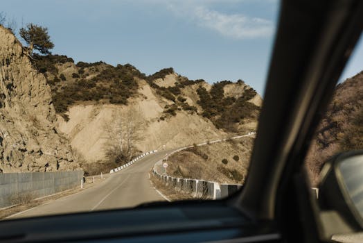 Driving along a winding mountain road with a view of rugged landscapes through the car window.
