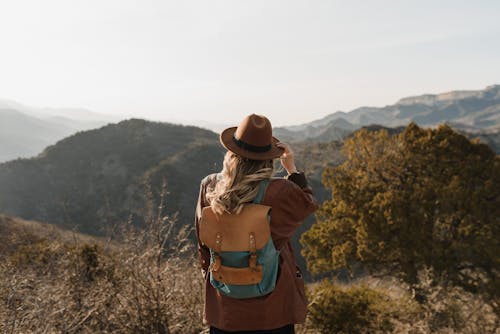 A Woman in Brown Jacket and Brown Backpack Standing on Brown Grass Field