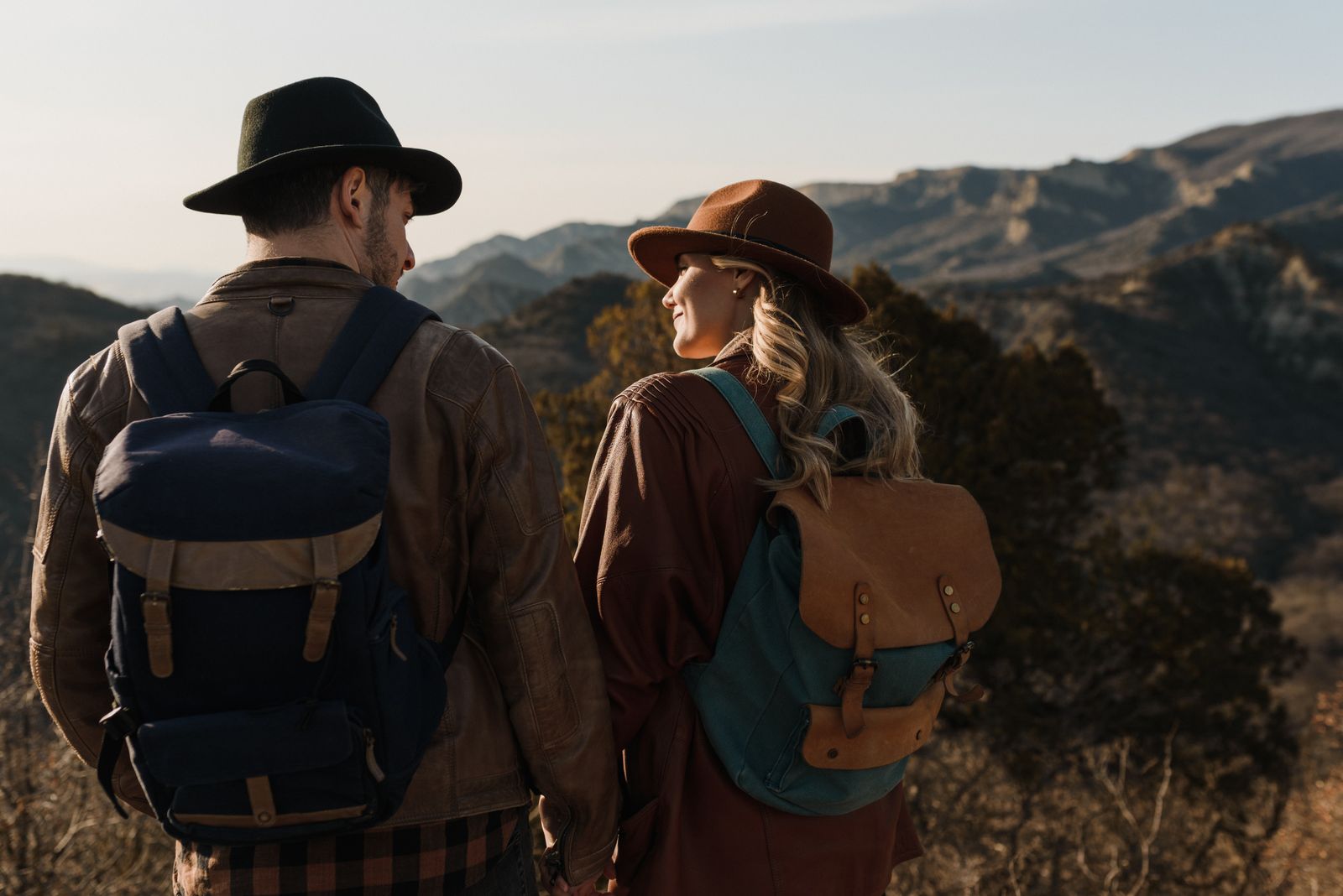 Two people wearing backpacks and hats with hills behind them