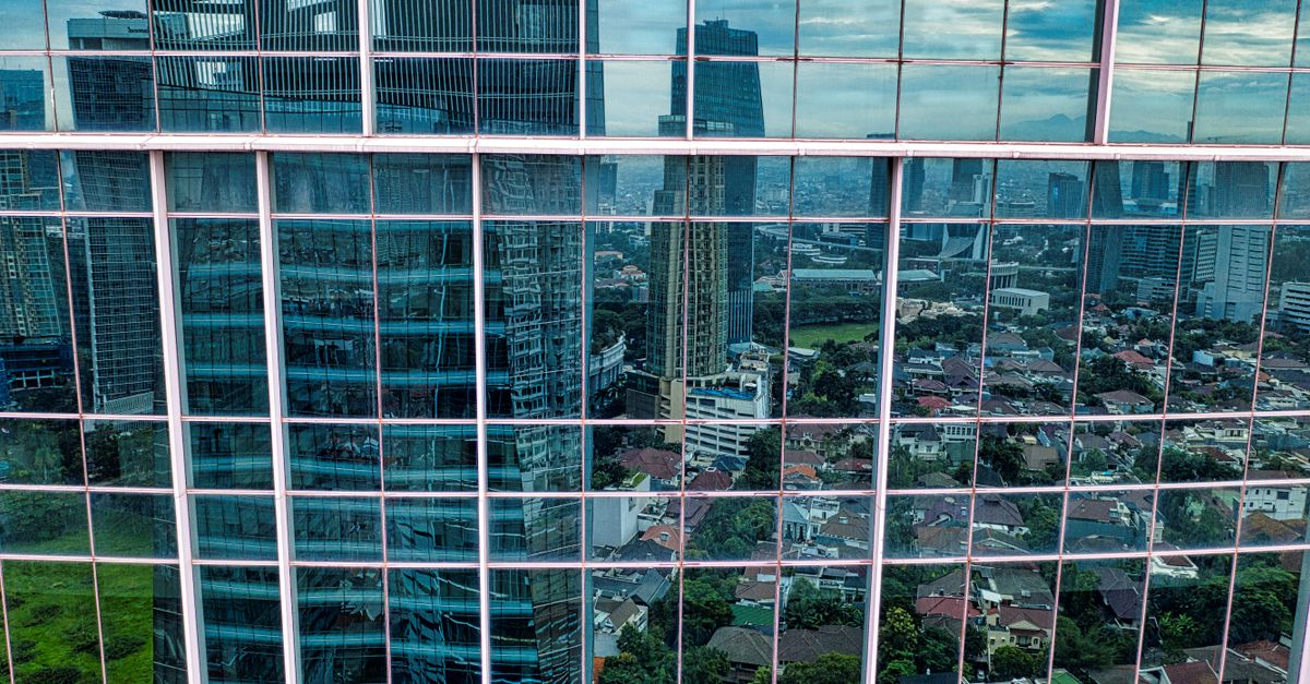 Reflection of Jakarta's urban skyline in a glass skyscraper, showcasing modern architecture and cityscape.
