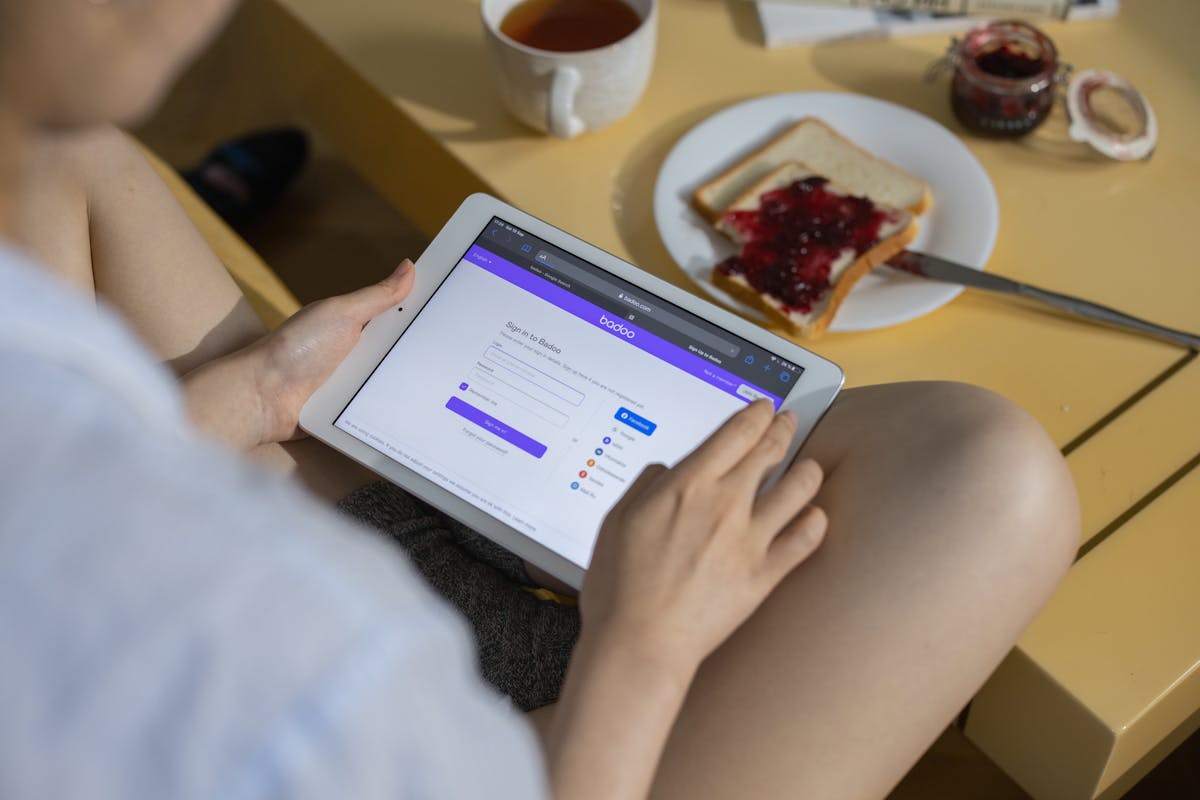 Person scrolling social media on a smartphone while sitting at a kitchen table with a drink