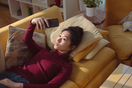 High-Angle Shot of a Woman in Maroon Sweater Lying on Sofa while Taking Photo of Herself Using a Cellphone