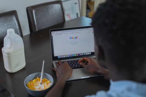 Free A person browsing Google on a laptop while having cereal breakfast at the table. Stock Photo