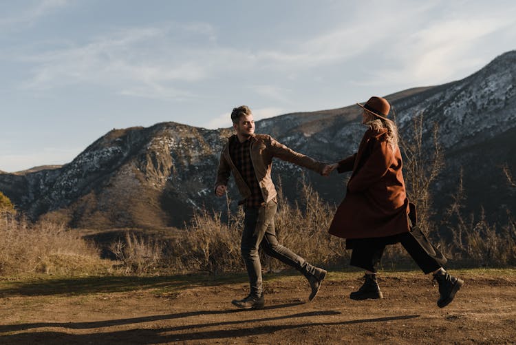 Man And Woman Running On Field Near Mountain