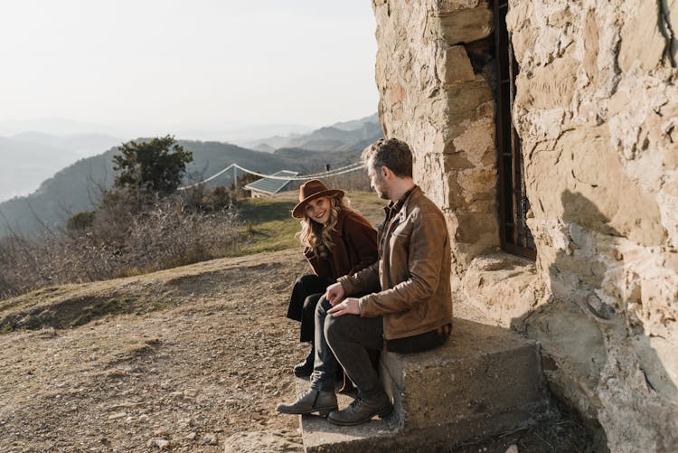 Man And Woman Sitting On The Steps Of A Building On Top Of A Hill 