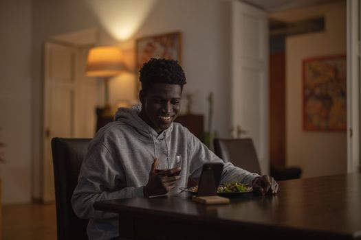 Smiling man having dinner and wine while using his smartphone indoors. Relaxed evening ambiance.