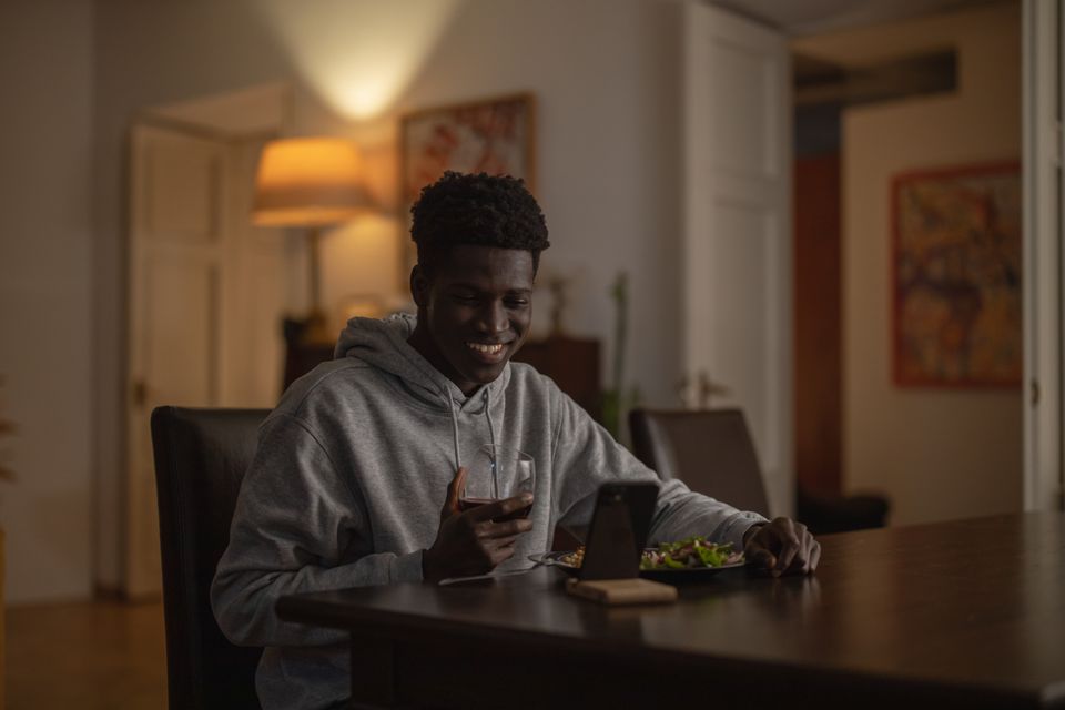 A smiling man having dinner and wine while looking at his phone