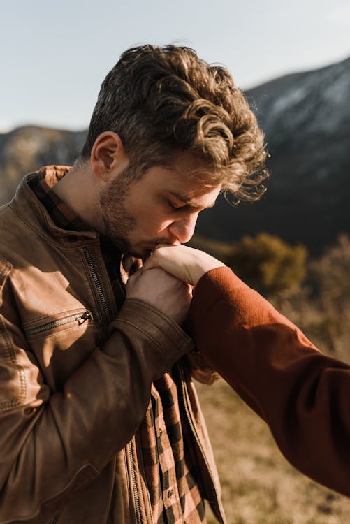 https://www.pexels.com/photo/young-man-kissing-girlfriend-hand-in-hilly-sunny-nature-7351063/