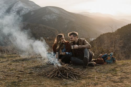 Free Couple enjoying a cozy bonfire with a thermos on a mountain top at sunset. Stock Photo