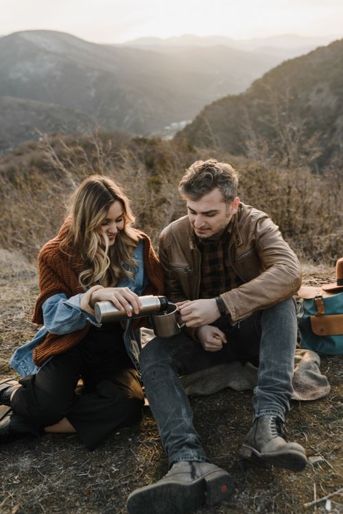 Free A couple sitting on a mountainside enjoying a hot drink together at sunset. Stock Photo