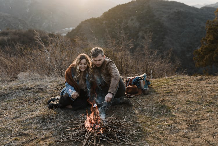 Man And Woman Grilling Marshmallows On Campfire In Mountains