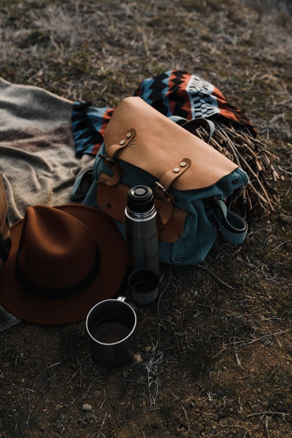 A Backpack, Thermos and a Hat Lying on a Picnic Blanket 