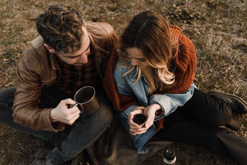 Free A couple sitting outdoors with cups, enjoying a warm drink and sharing a romantic moment. Stock Photo