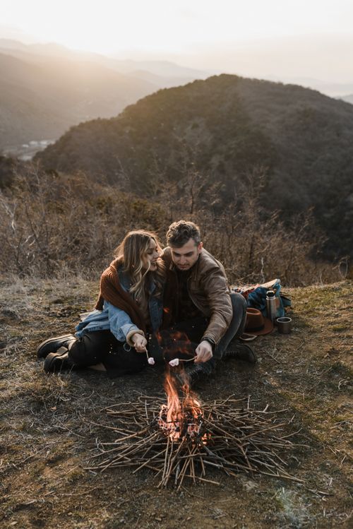 Free A couple enjoys roasting marshmallows by a campfire on a mountain at sunset. Stock Photo