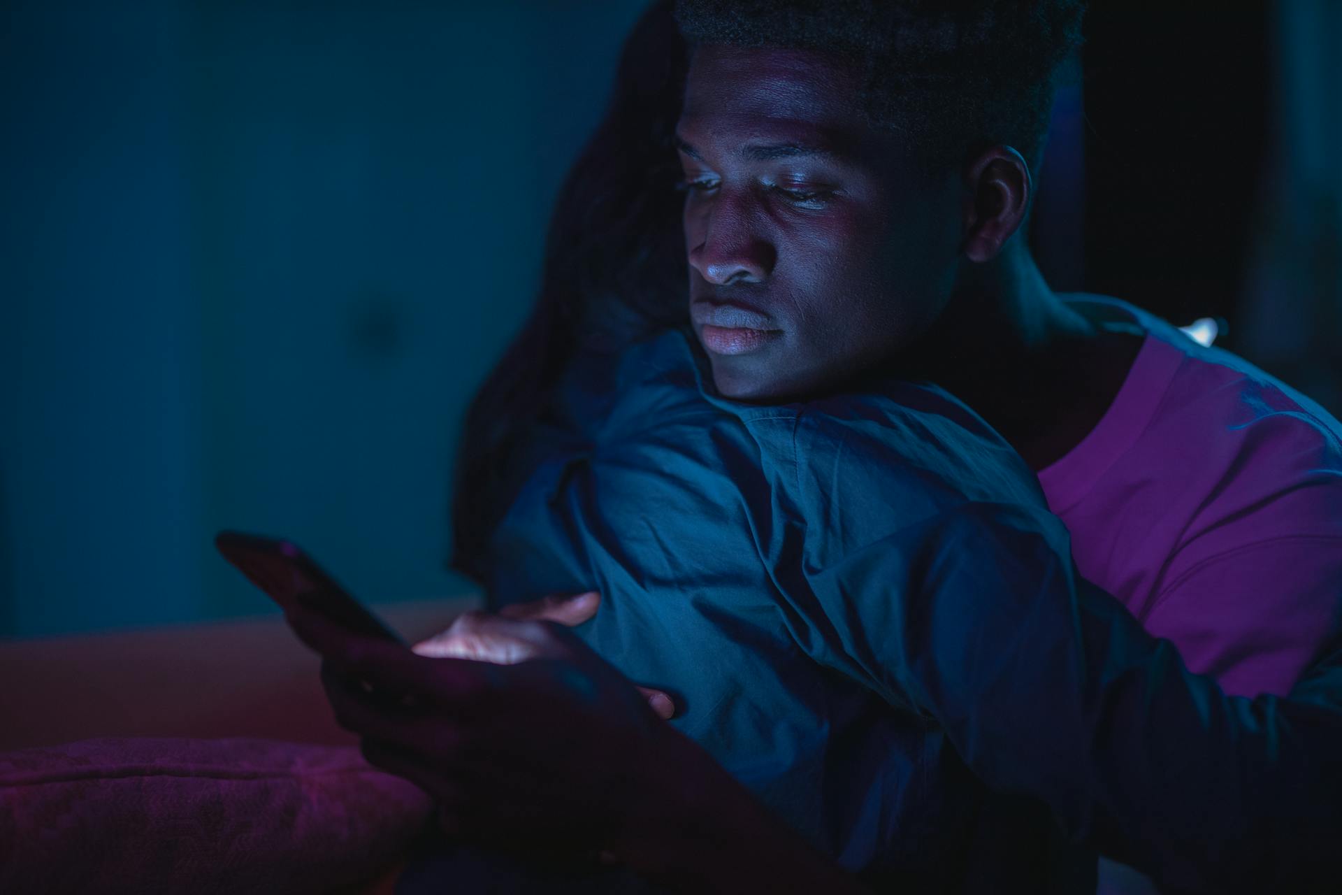 African American couple embracing at night while using a smartphone, conveying intimacy and modern technology.