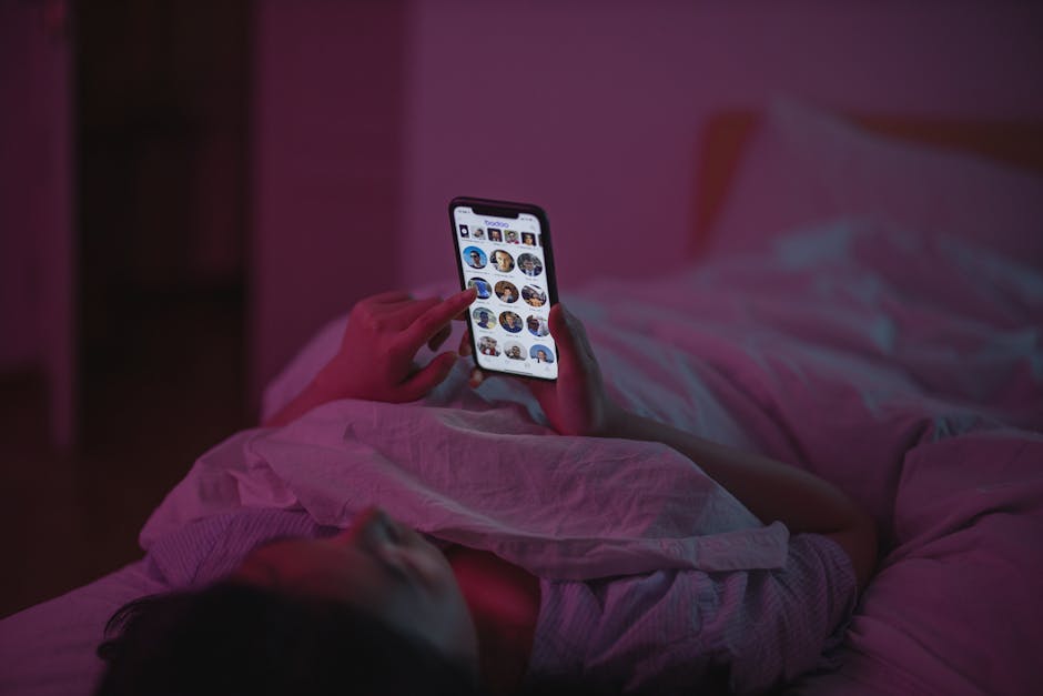 What Research Reveals About Oura Ring Sleep Staging Accuracy A woman relaxes in bed at night, browsing on her smartphone under pink ambient lighting.