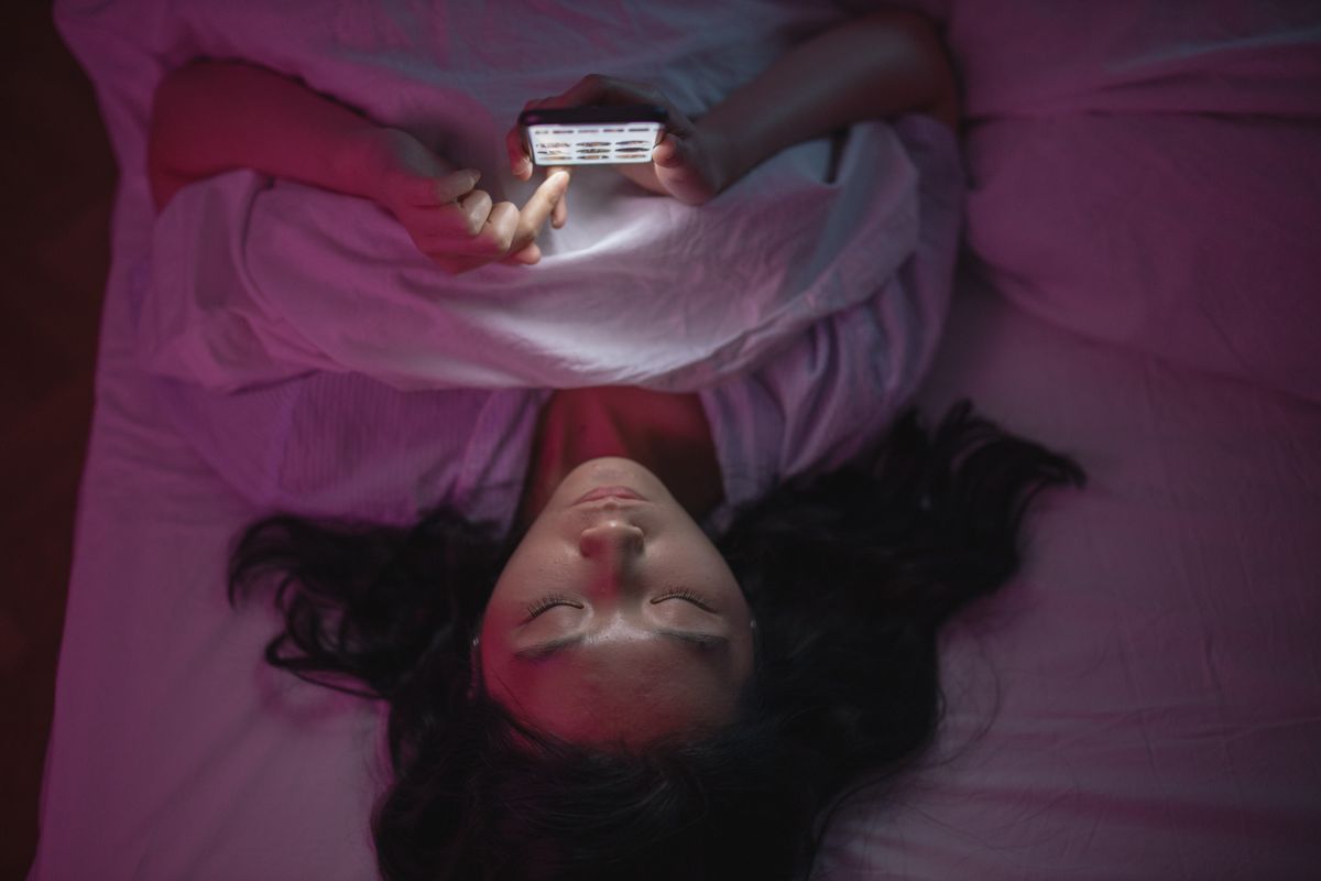 Woman lying in bed browsing her smartphone at night