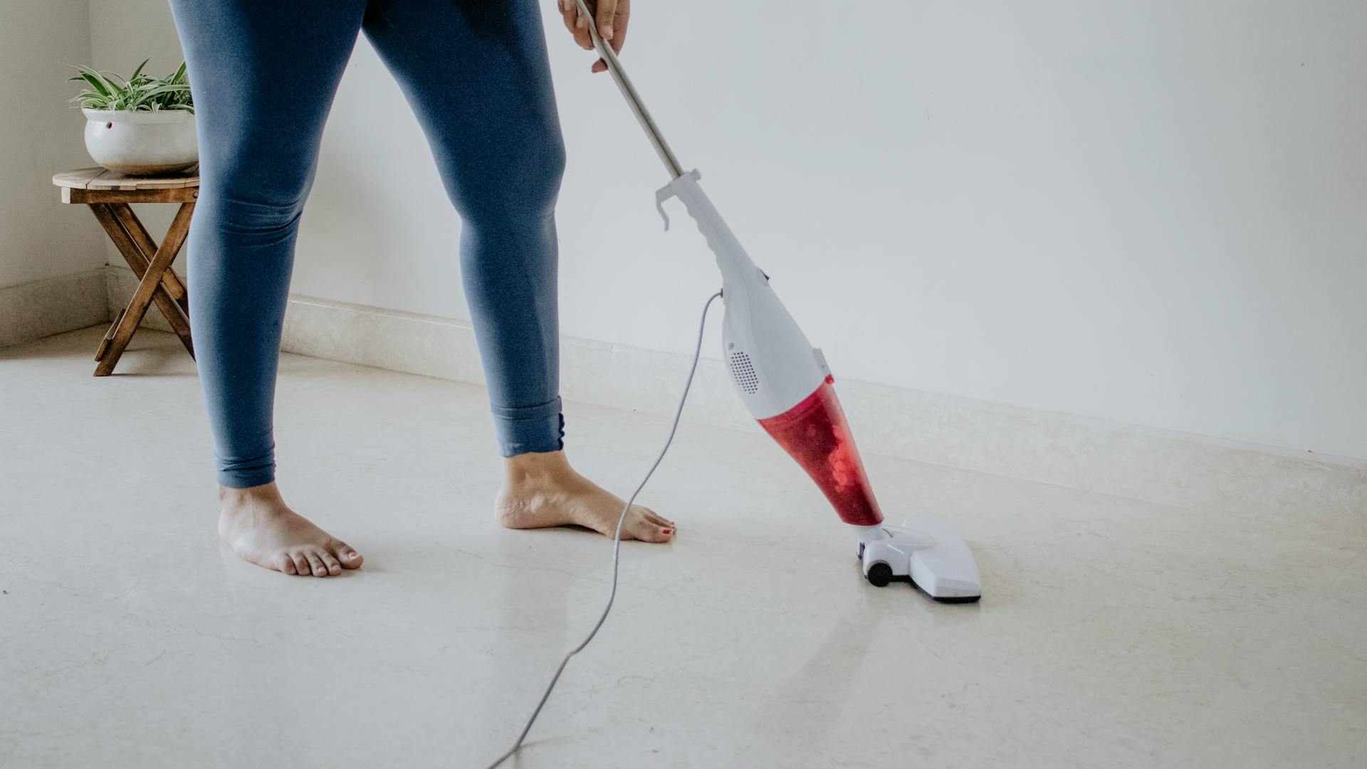 Close-up of a woman vacuuming a clean marble floor barefoot, showcasing home cleaning and maintenance.