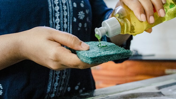 A Person Pouring Dishwashing Soap On A Scrub Pad