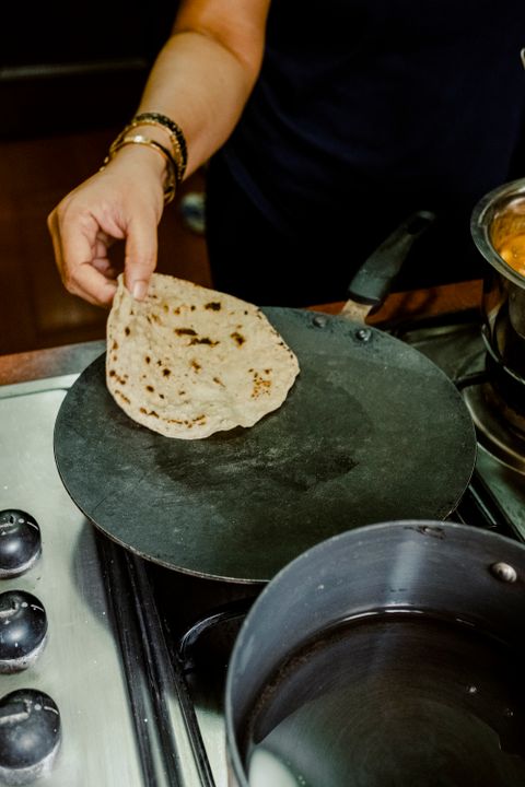 The Science Behind Roti: Why It Stays Soft or Goes Hard (Explained Simply) 1 Hands placing a chapati onto a hot tava over a gas stove, showing the traditional cooking process.