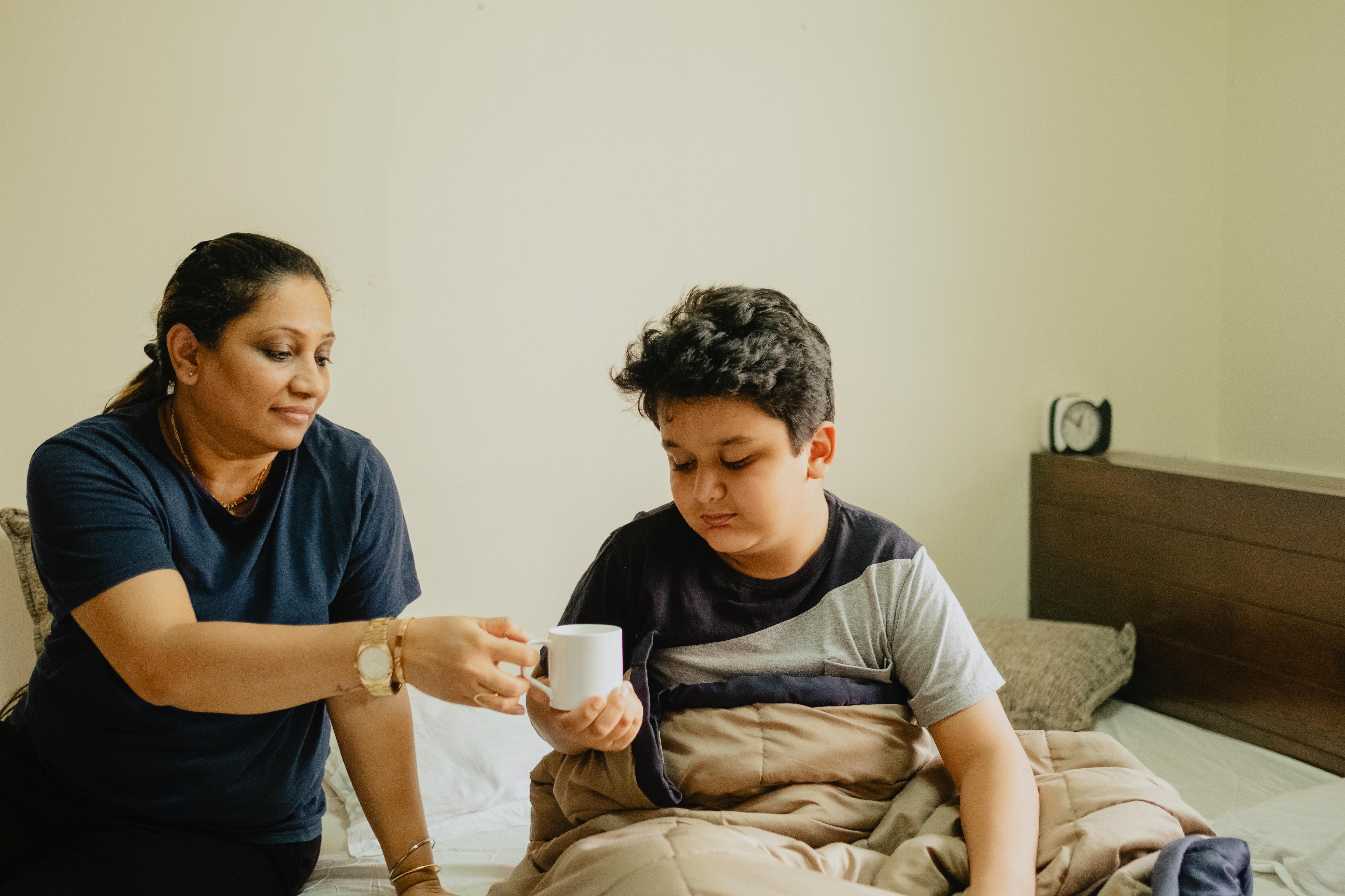 woman giving a boy drink on white mug