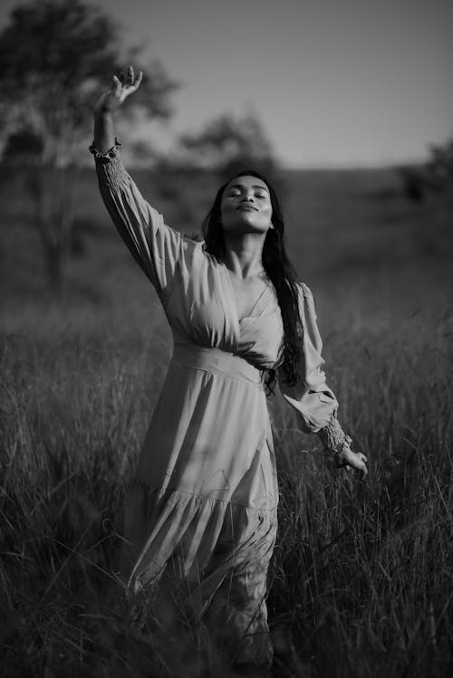Grayscale Photo of Woman in Dress Standing on Grass Field