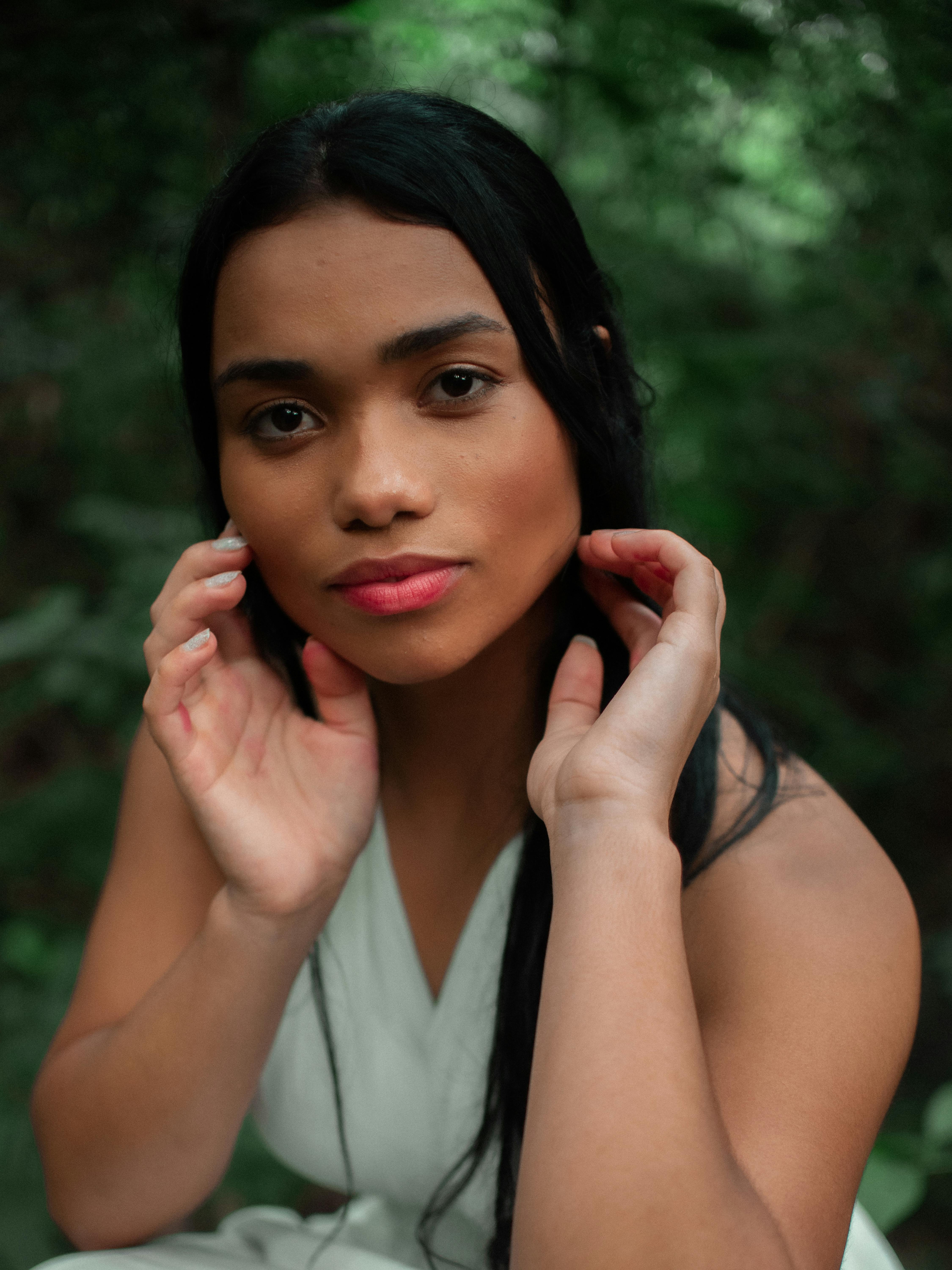 Close-up portrait of a woman in a natural setting, wearing a white top.