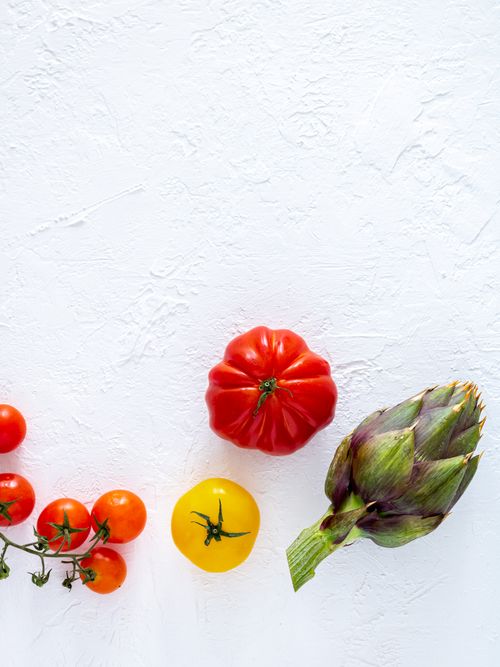 Free Overhead view of fresh tomatoes and artichoke on a white textured background Stock Photo