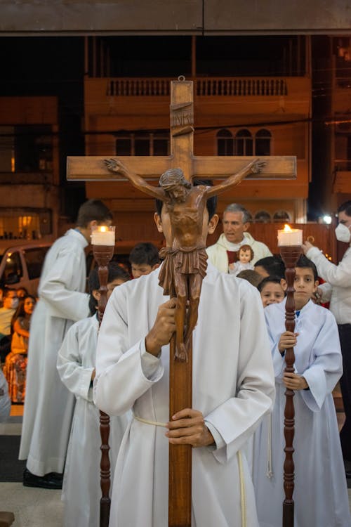 Person in White Standing Holding a Wooden Crucifix