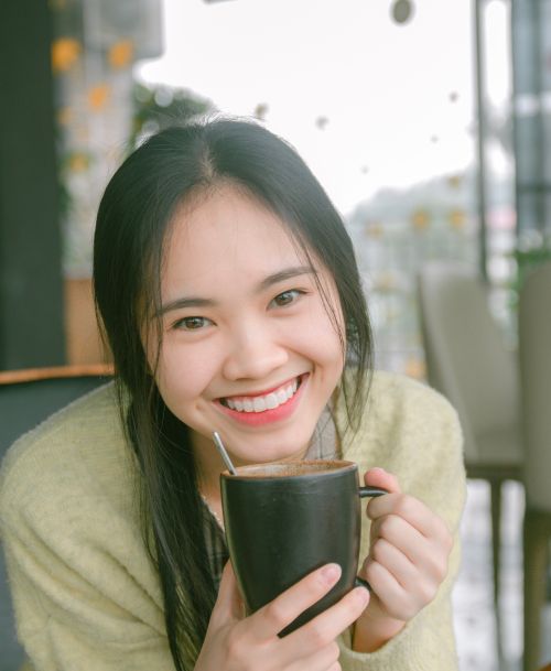 Free Smiling woman holding a cup of coffee in a warm cafe setting. Stock Photo