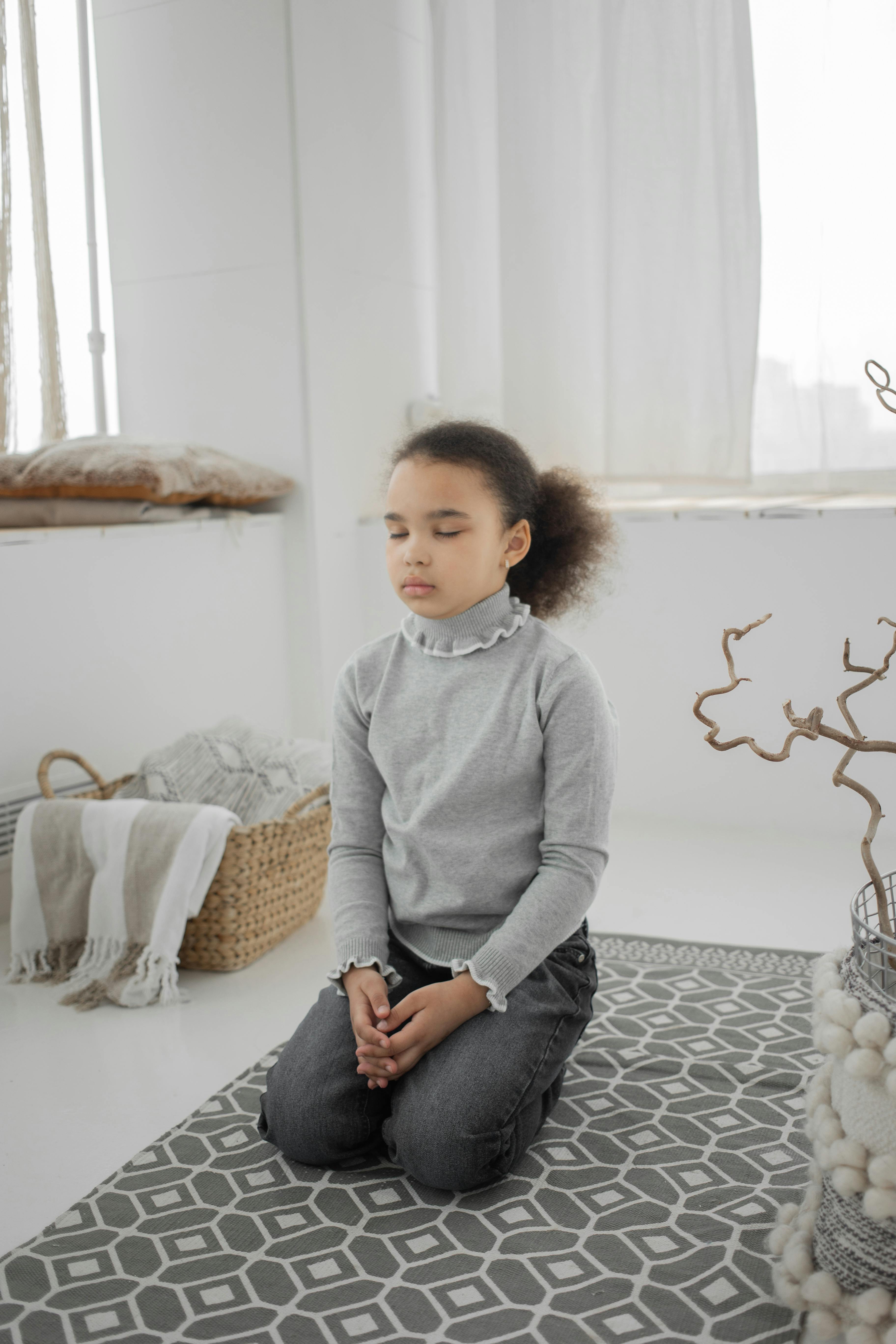 Free Young girl in calm meditation on a rug in a bright cozy room, eyes closed in tranquility. Stock Photo