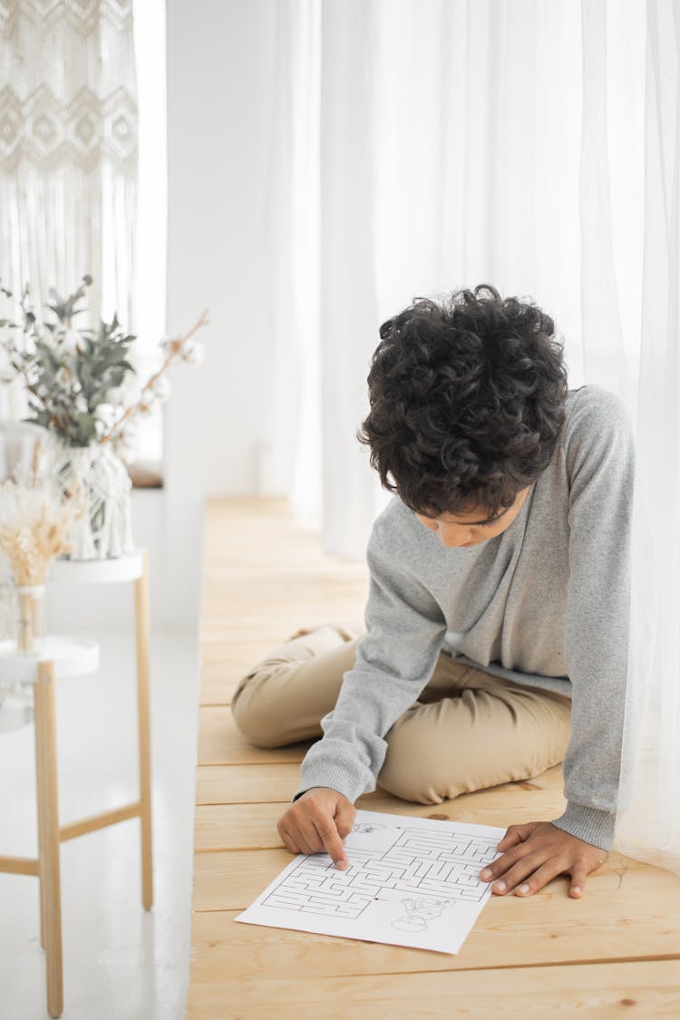 Serious Little Ethnic Child Solving Painted Labyrinth On Windowsill At Home