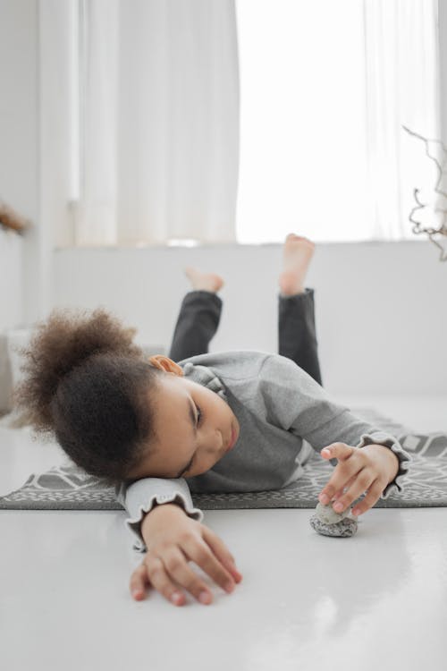 Bored little African American girl lying on floor and stacking stones