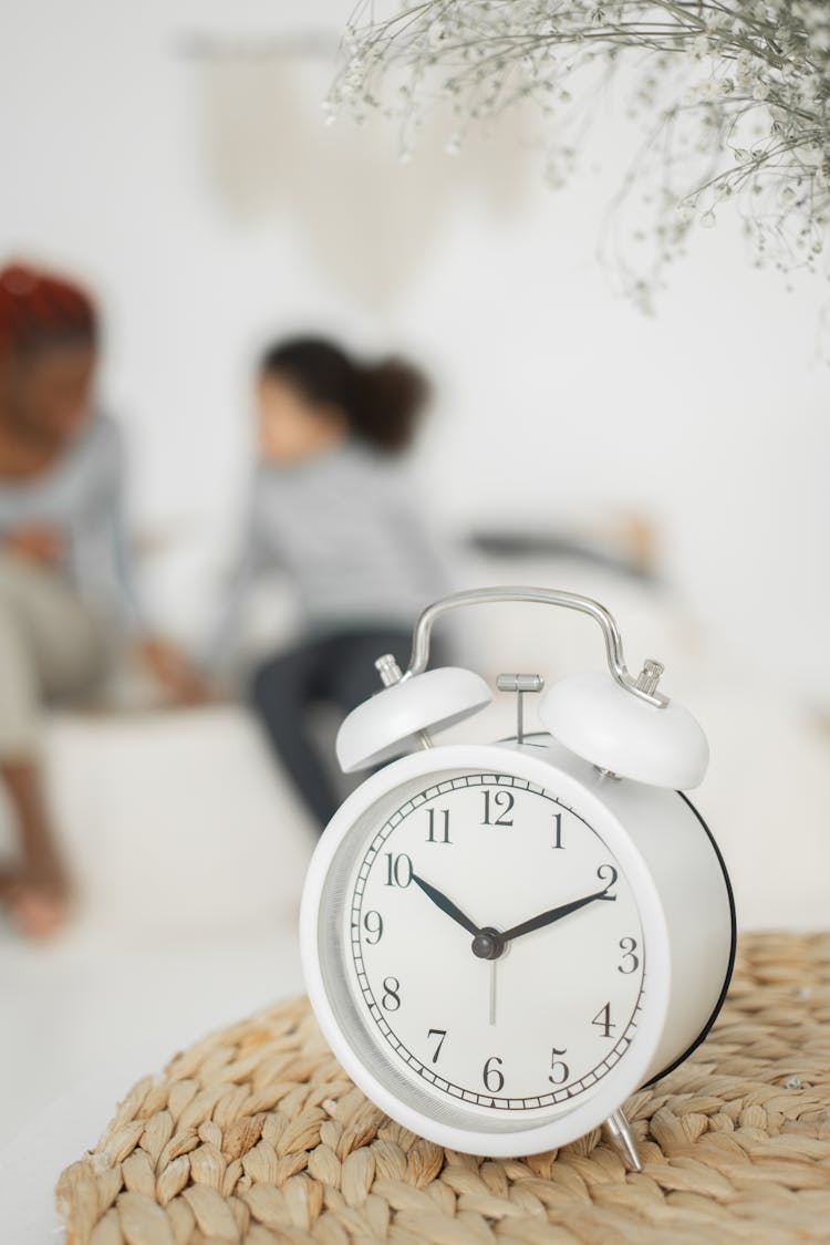 Anonymous Black Woman With Daughter Sitting On Bed Near Retro Alarm Clock