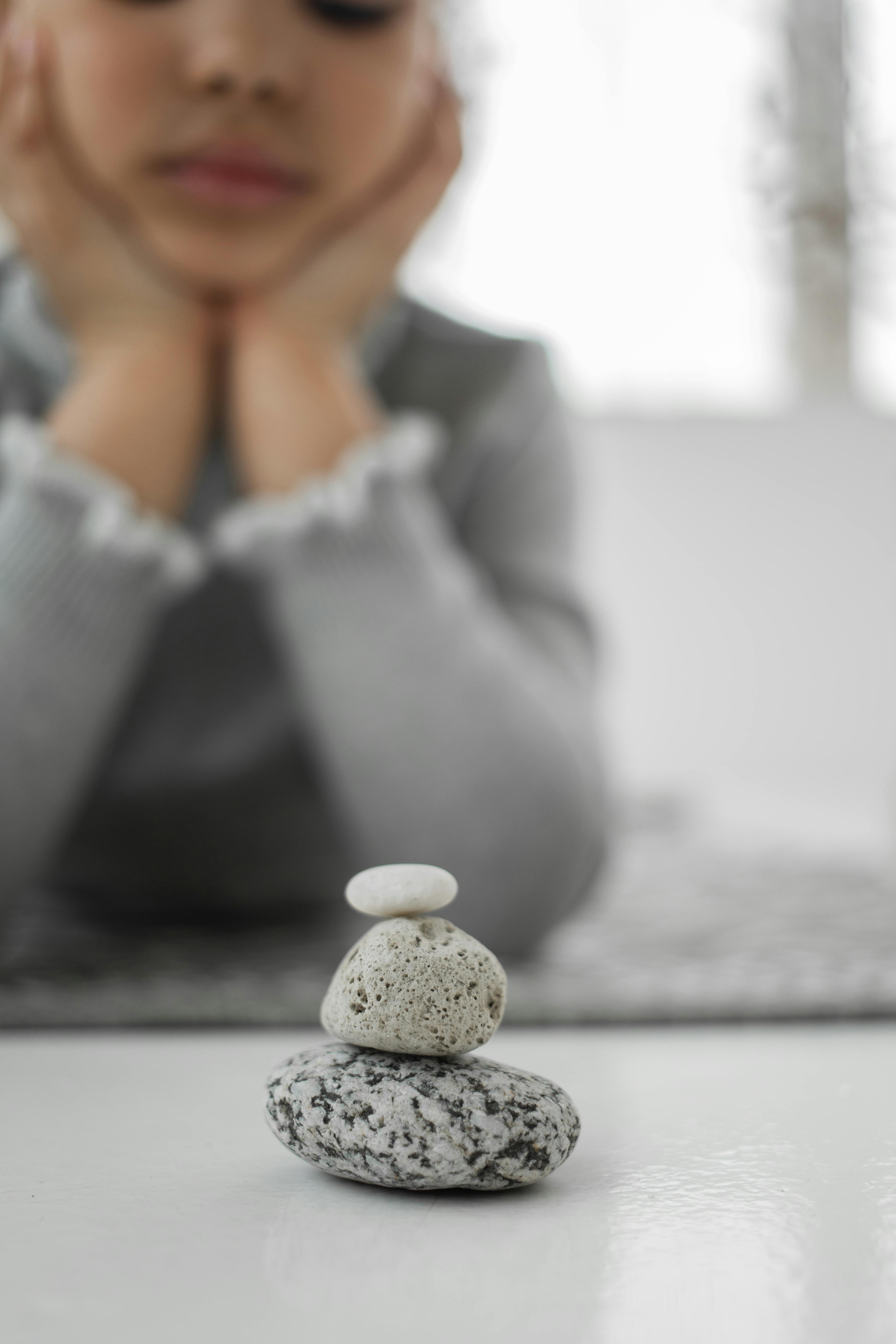 pensive little ethnic girl lying on floor and looking at stones stack