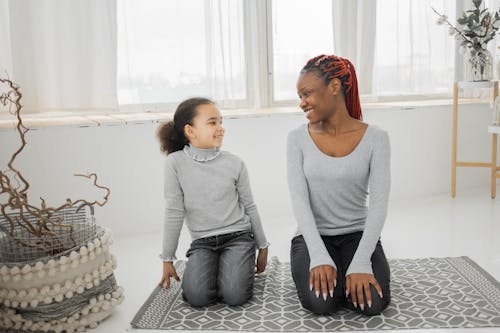 Smiling black mother with daughter sitting on floor and looking at each other