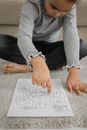 From above of crop attentive little black girl in casual clothes passing path of logic labyrinth game with finger sitting on floor at home