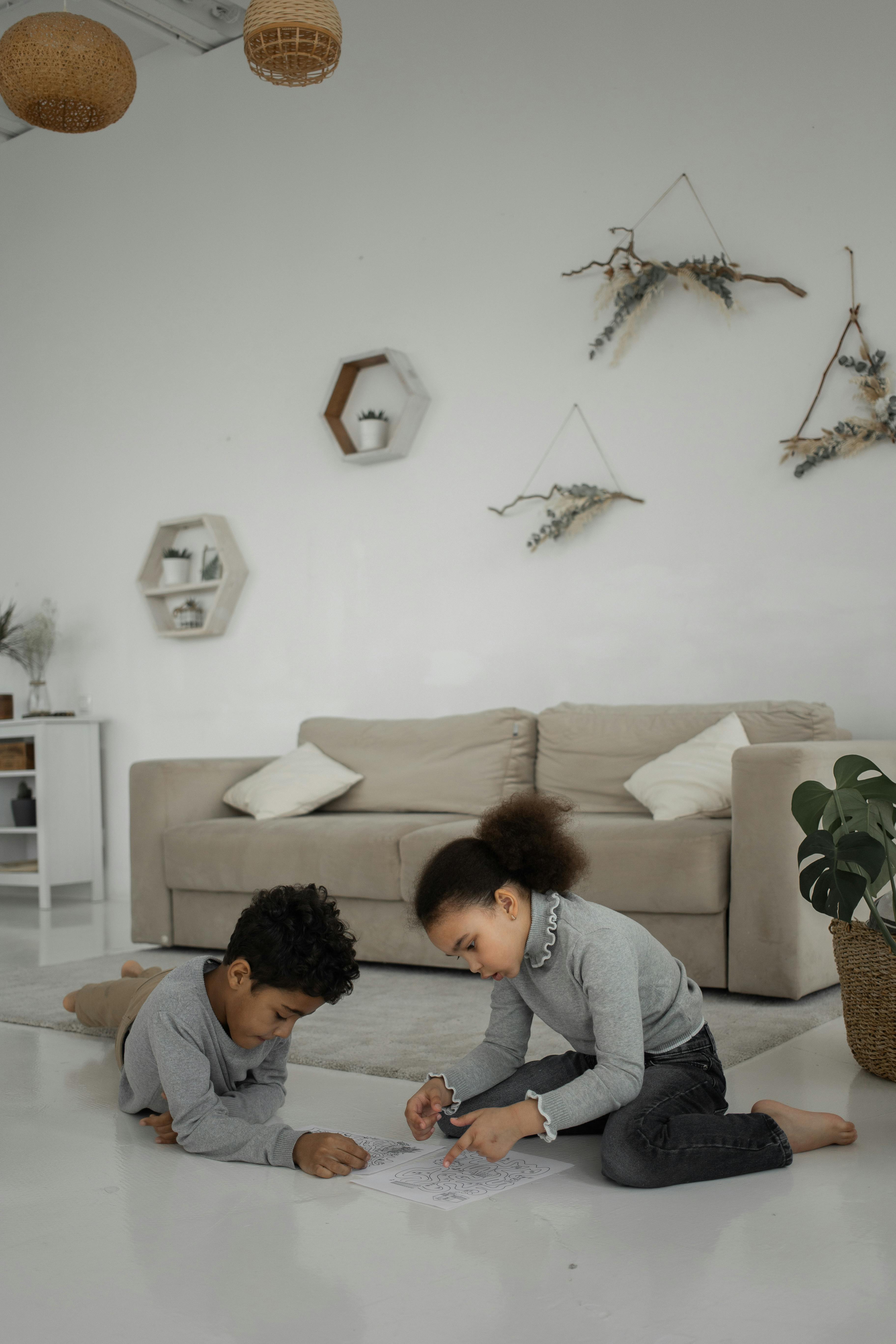 smart little ethnic siblings solving maze task on floor at home