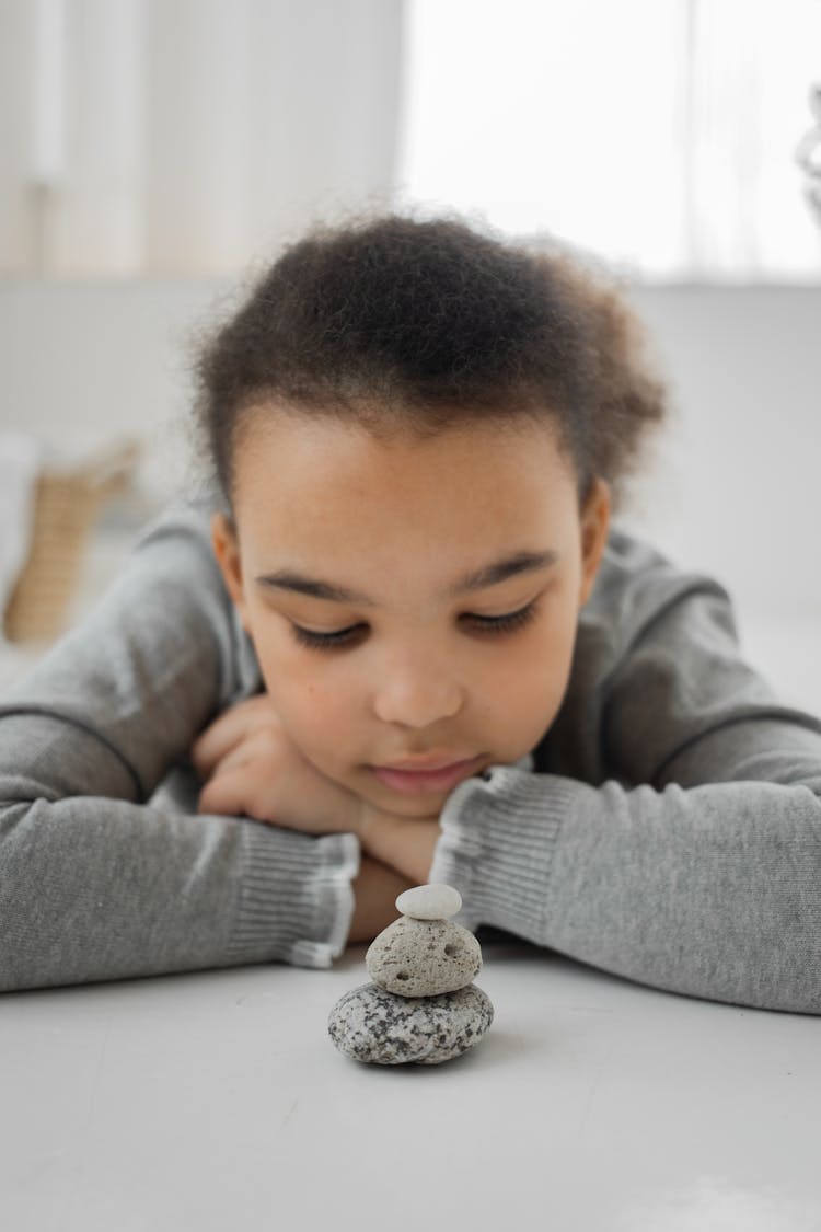 Peaceful Little Ethnic Kid Lying On Floor While Playing With Balancing Stones