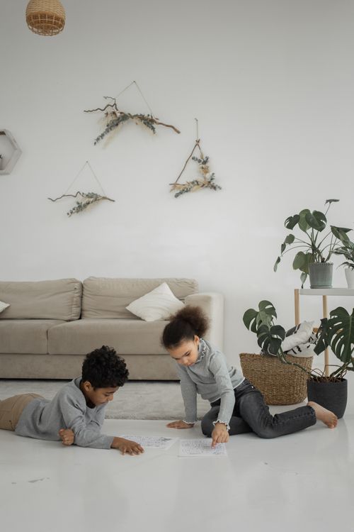 Free Adorable little African American siblings with dark curly hair in similar clothes sitting on floor in living room and playing Stock Photo