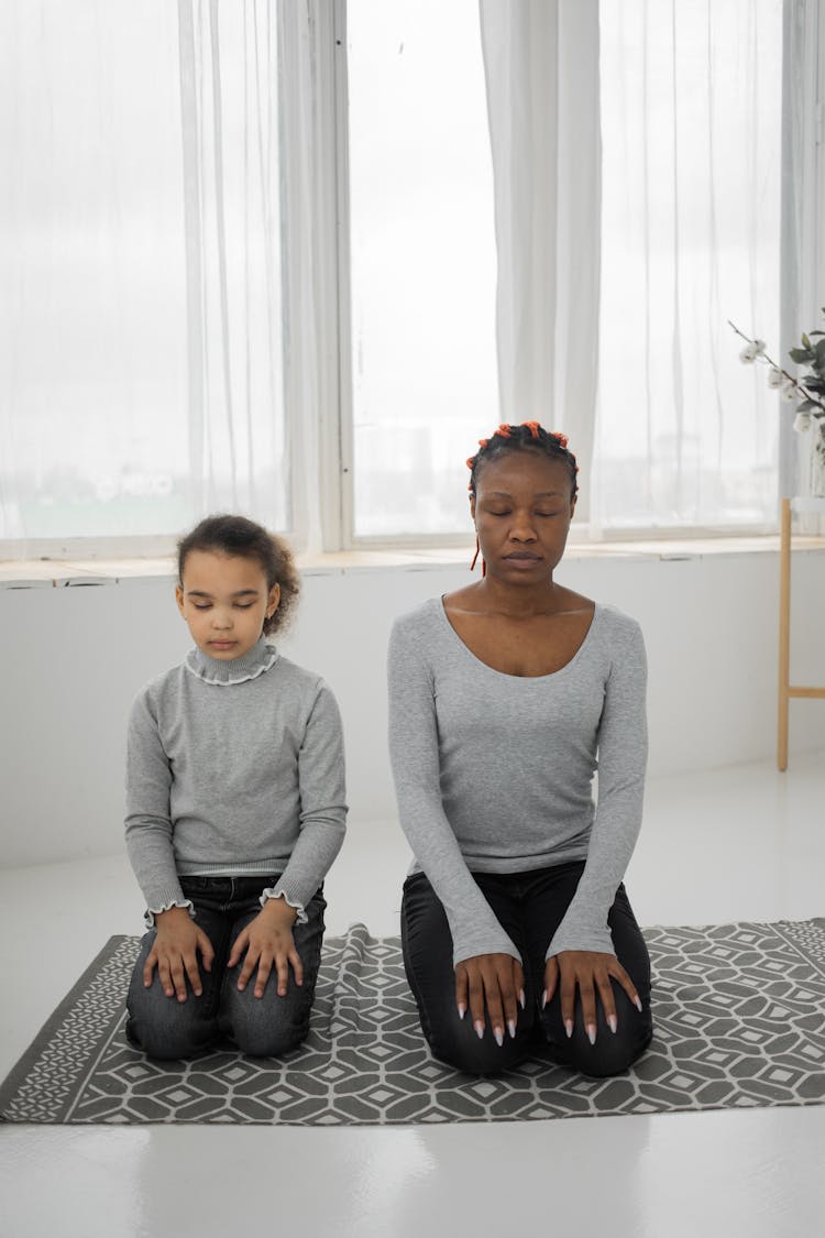 Calm Black Young Mother With Daughter Meditating With Closed Eyes At Home