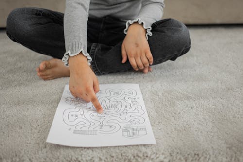 Free Crop anonymous barefooted child sitting on floor with crossed legs and solving labyrinth puzzle at home Stock Photo