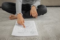 Crop anonymous barefooted child sitting on floor with crossed legs and solving labyrinth puzzle at home
