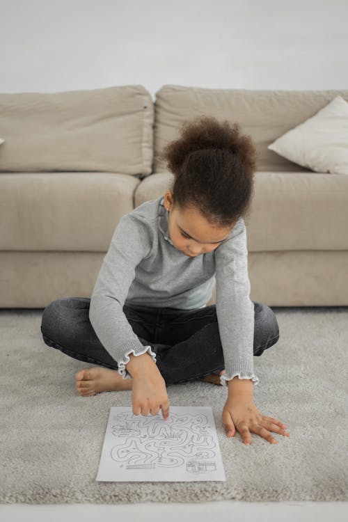 Free Concentrated black kid sitting on floor and and solving logical exercise Stock Photo