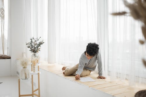 Concentrated little black kid doing homework on windowsill