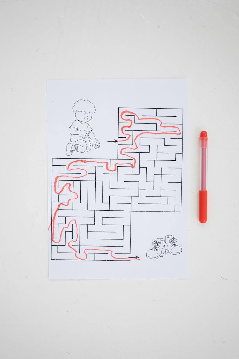 Top view of solved labyrinth test with little boy and boots painted on paper placed on white desk with red pen